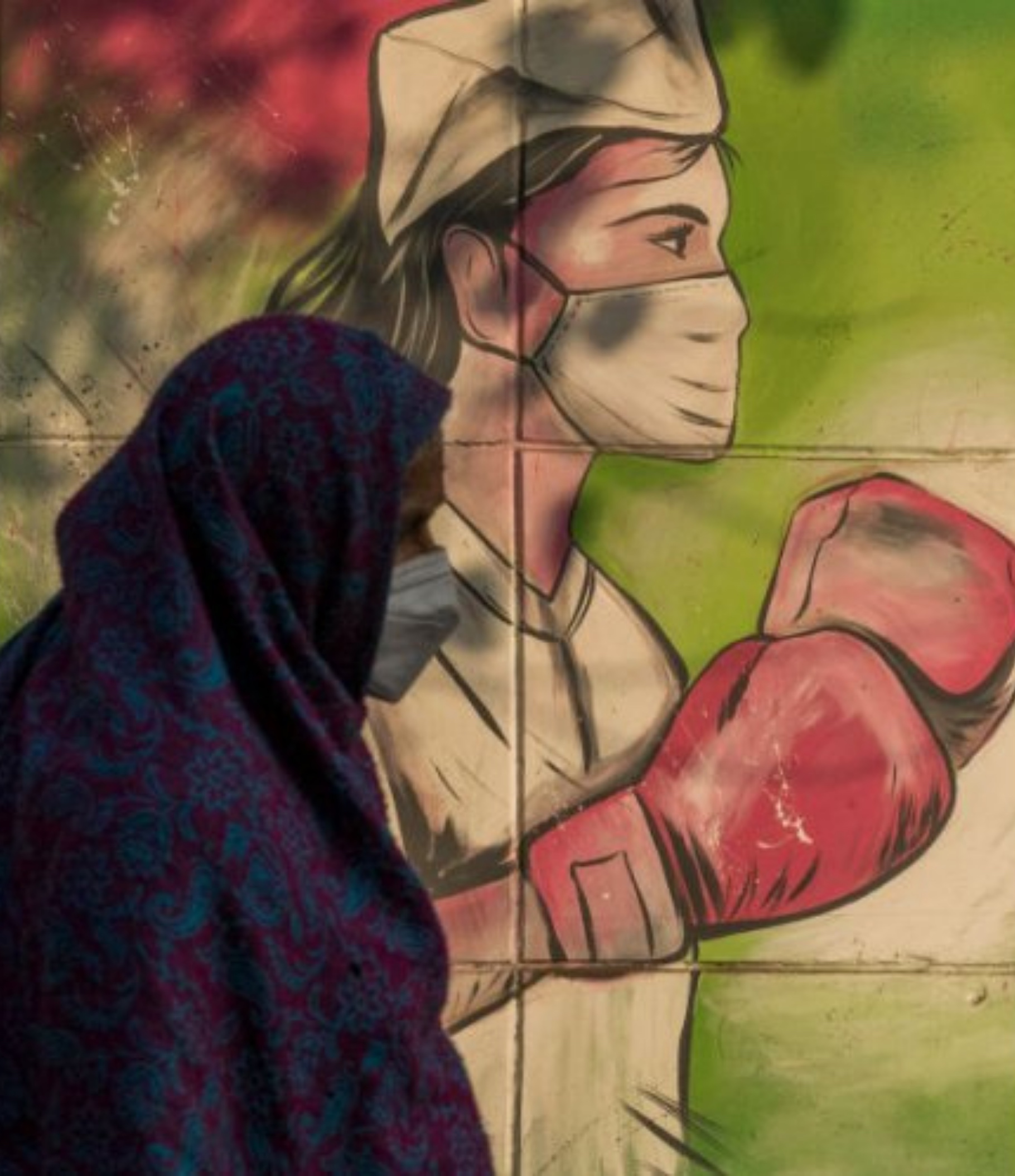 A woman wearing a facemask walks past a mural referring to the Covid-19 coronavirus in New Delhi, India