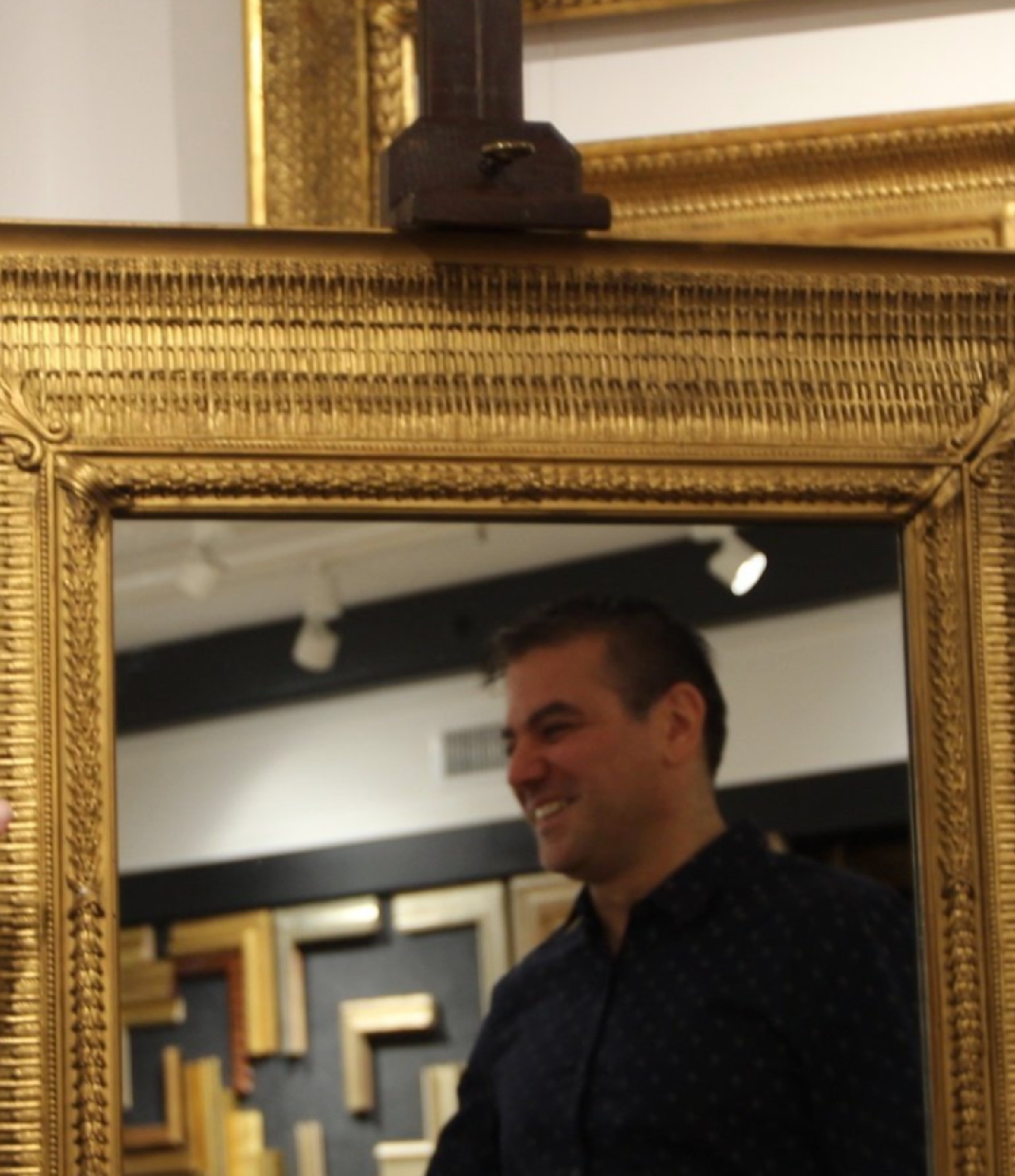 A gilded framed mirror reflecting a man's face